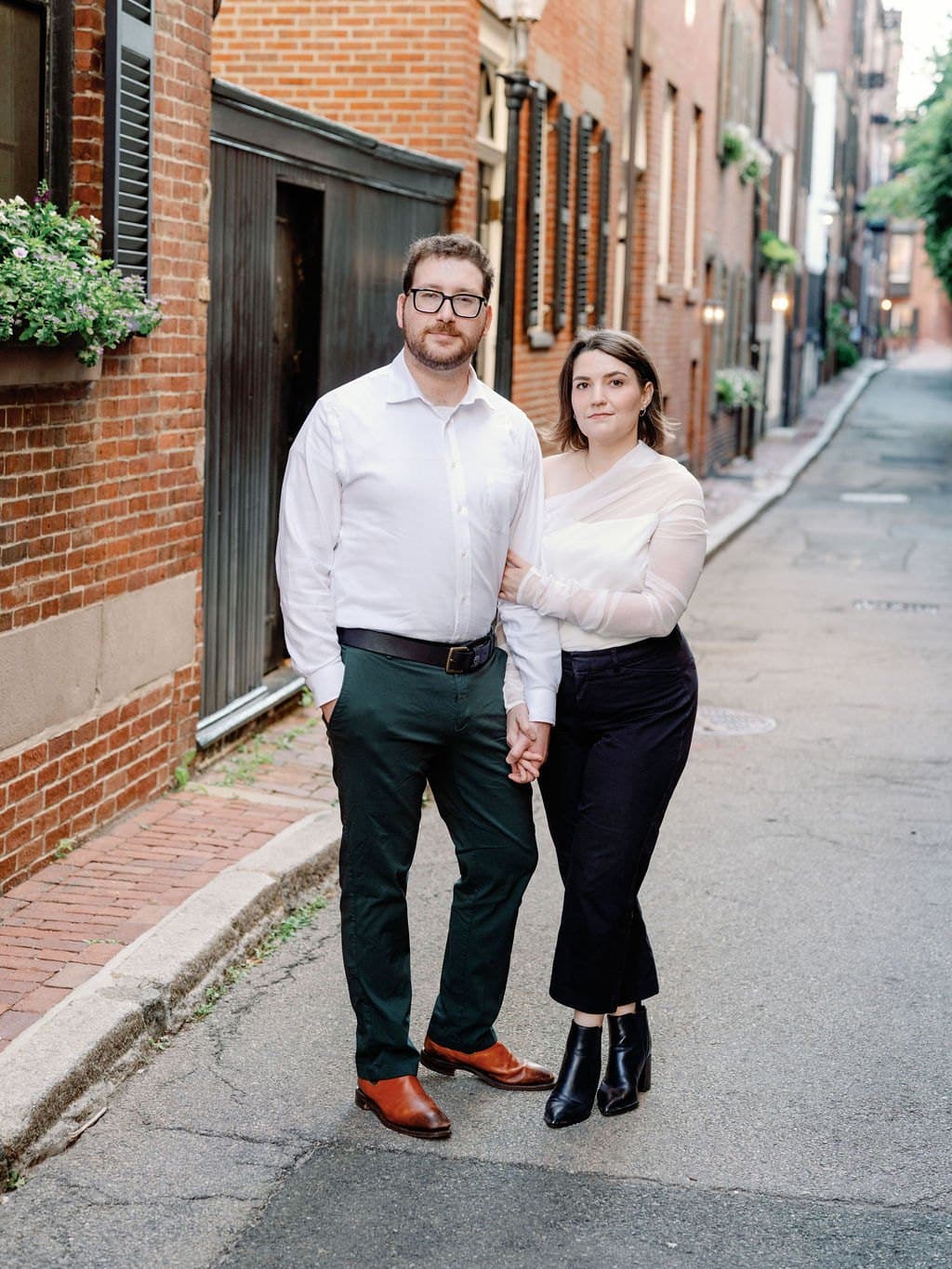 An engaged couple holding hands on a brick lined Beacon Hill street in Boston