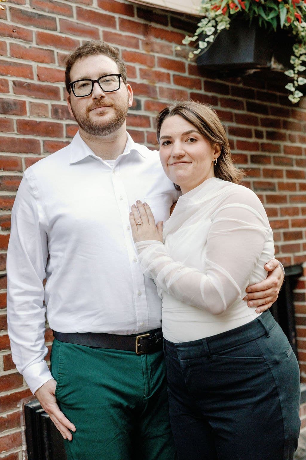 Engaged couple standing together against a brick wall on a city block