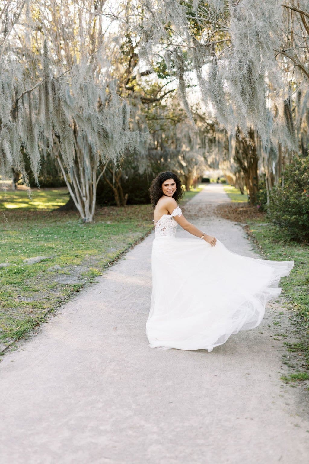 A bride twirling her tulle skirt on a path beneath Spanish moss in Charleston
