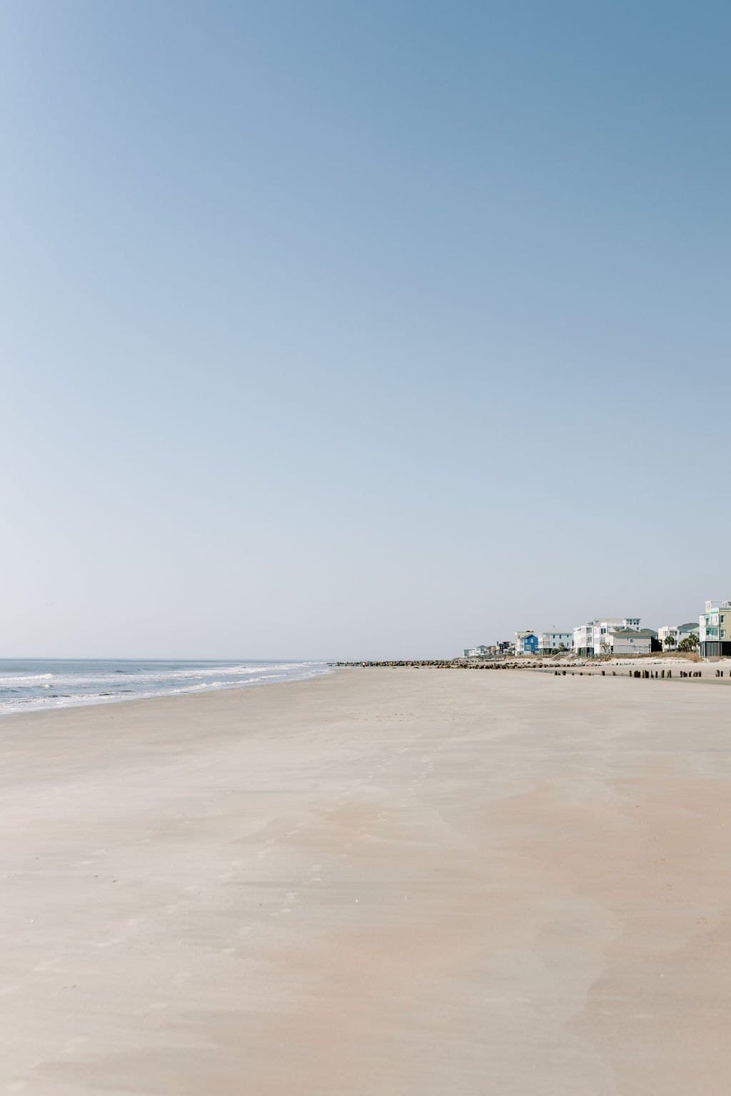 An empty stretch of beach and shoreline houses under a clear sky near Charleston
