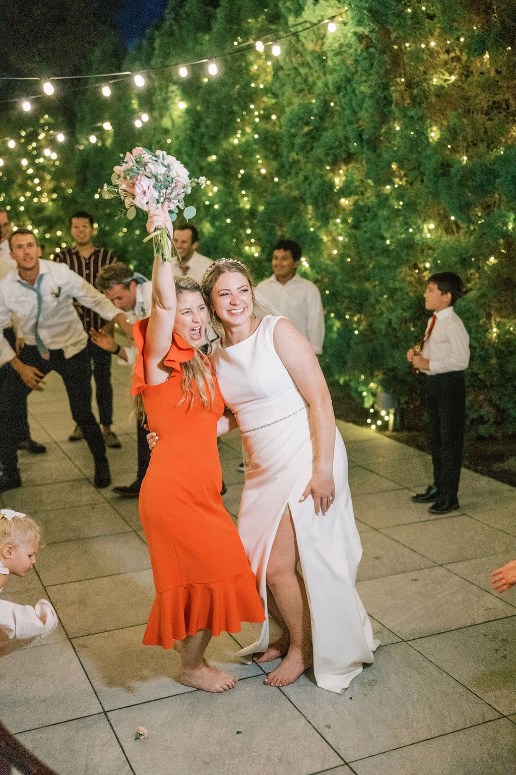 Bride and a guest celebrating together on the dance floor under string lights