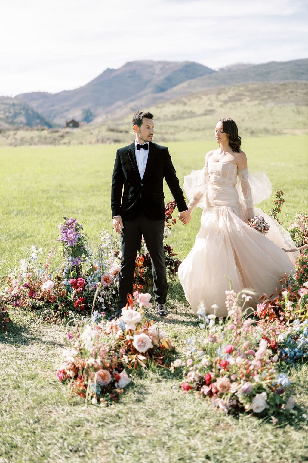 Bride and groom walking a mountain meadow through scattered florals