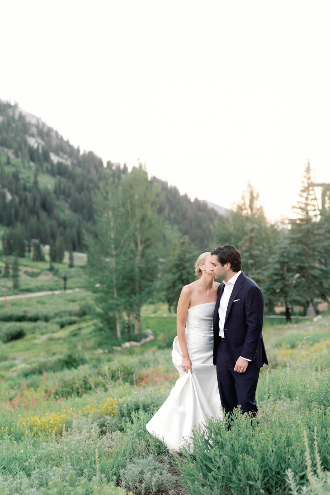A bride and groom kissing in a mountain meadow at dusk