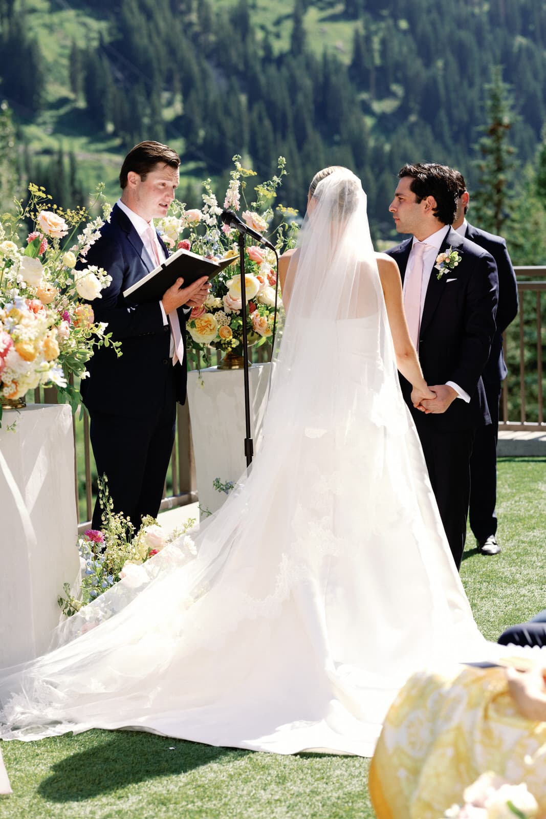 A bride in a long veil holding her groom's hand during vows at a mountain ceremony