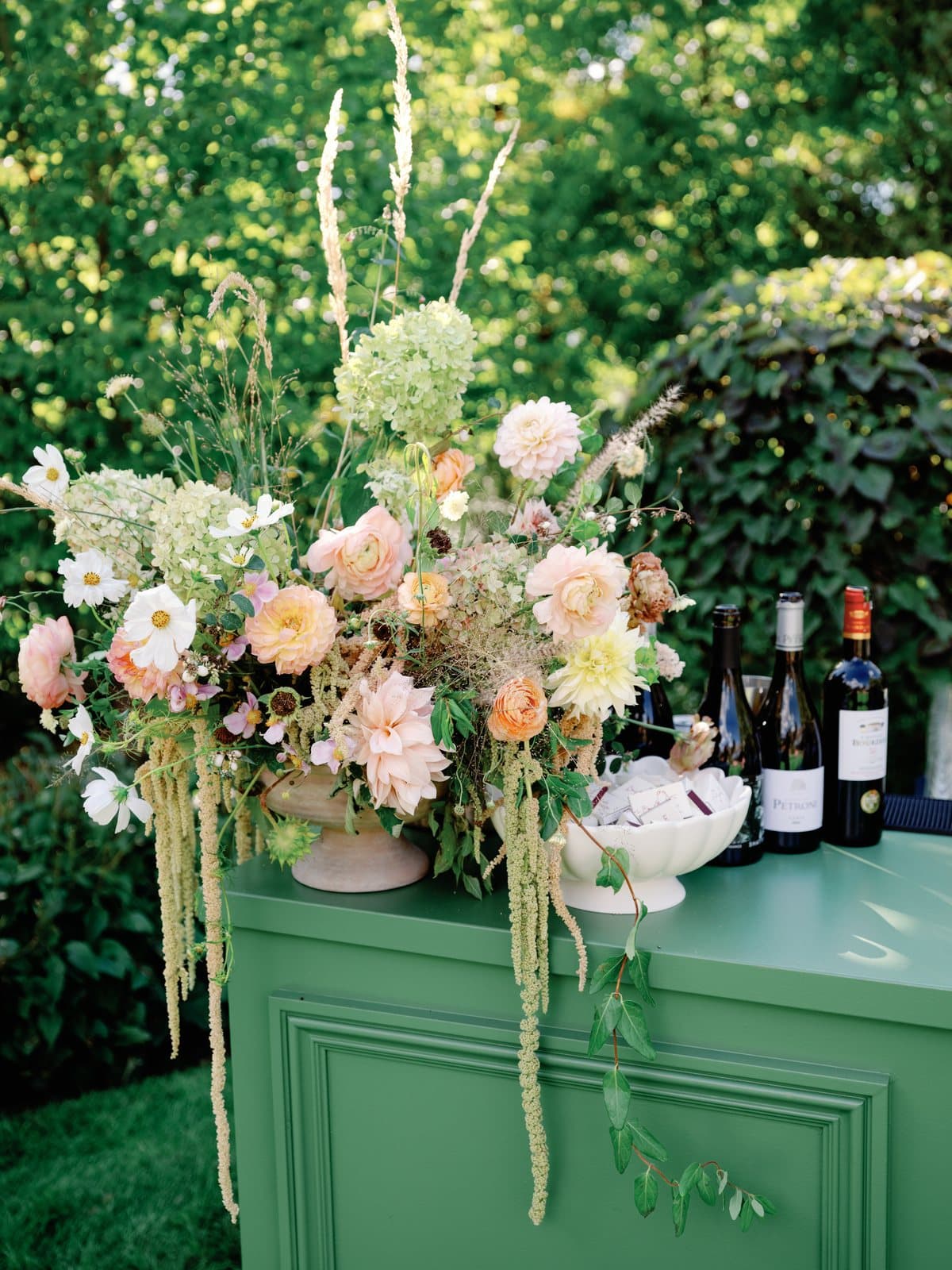 Peach dahlias, ranunculus and trailing amaranthus spilling over a green bar at a garden wedding