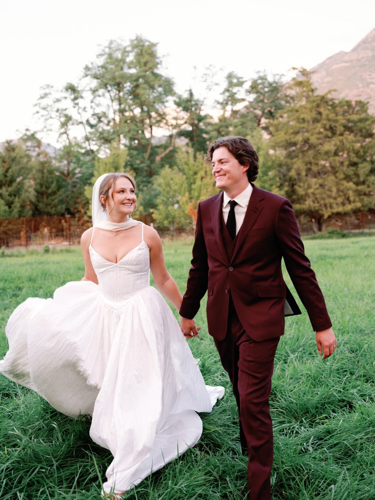 A bride and groom walking hand in hand through a mountain meadow, her skirt swinging