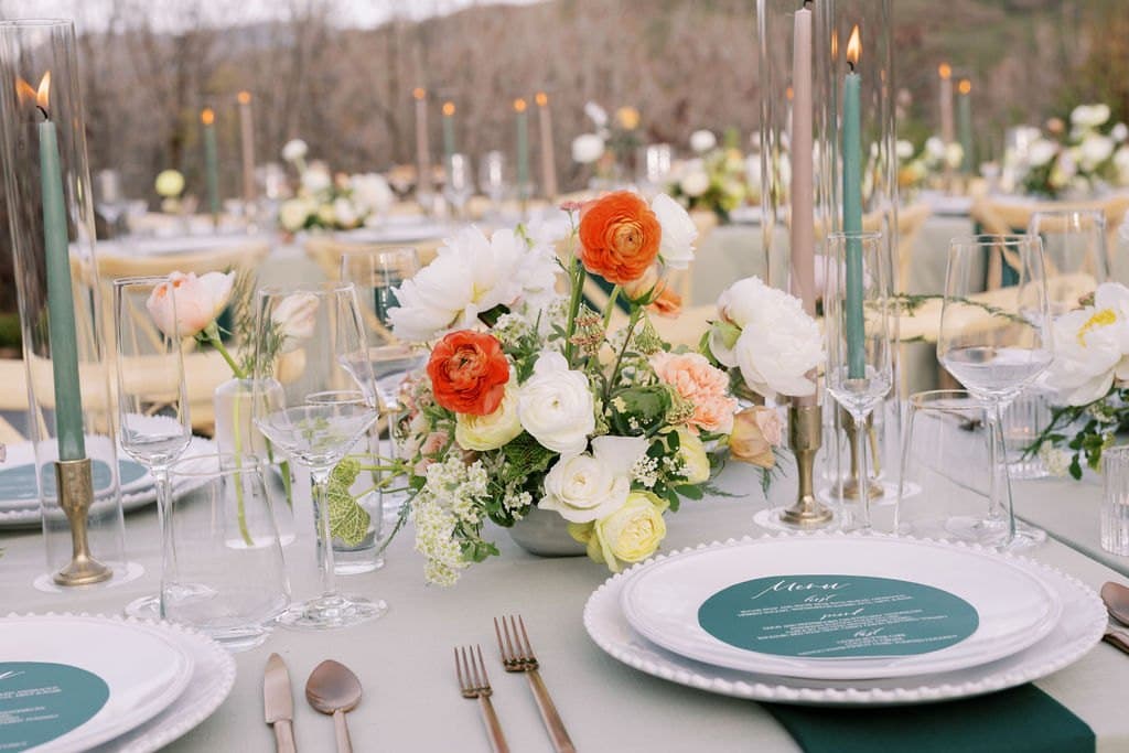 A reception tablescape with orange and white florals, green taper candles and a menu card at a Park City wedding