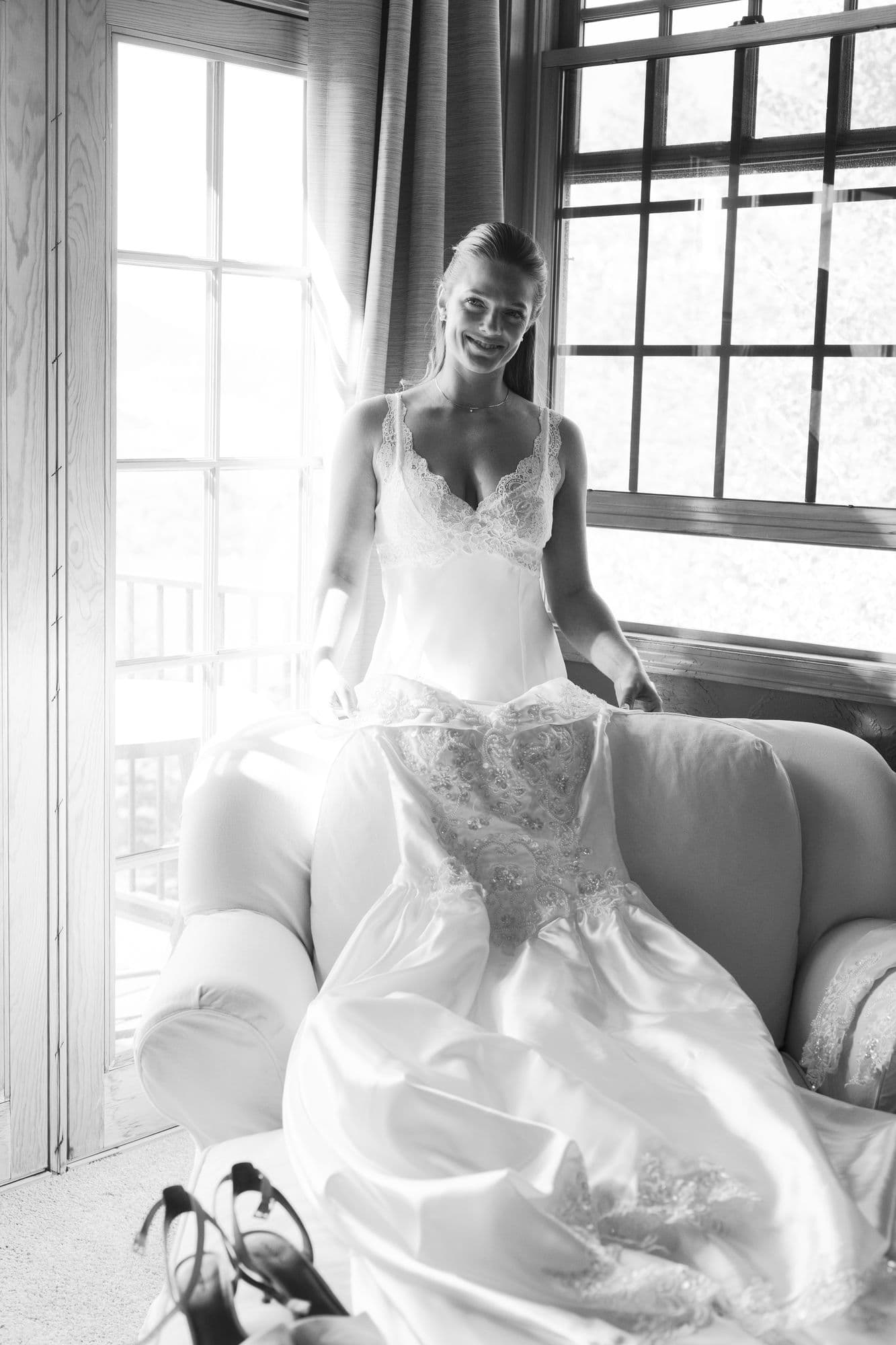 Marita seated in a tall window in her wedding gown, morning light across the room, in black and white