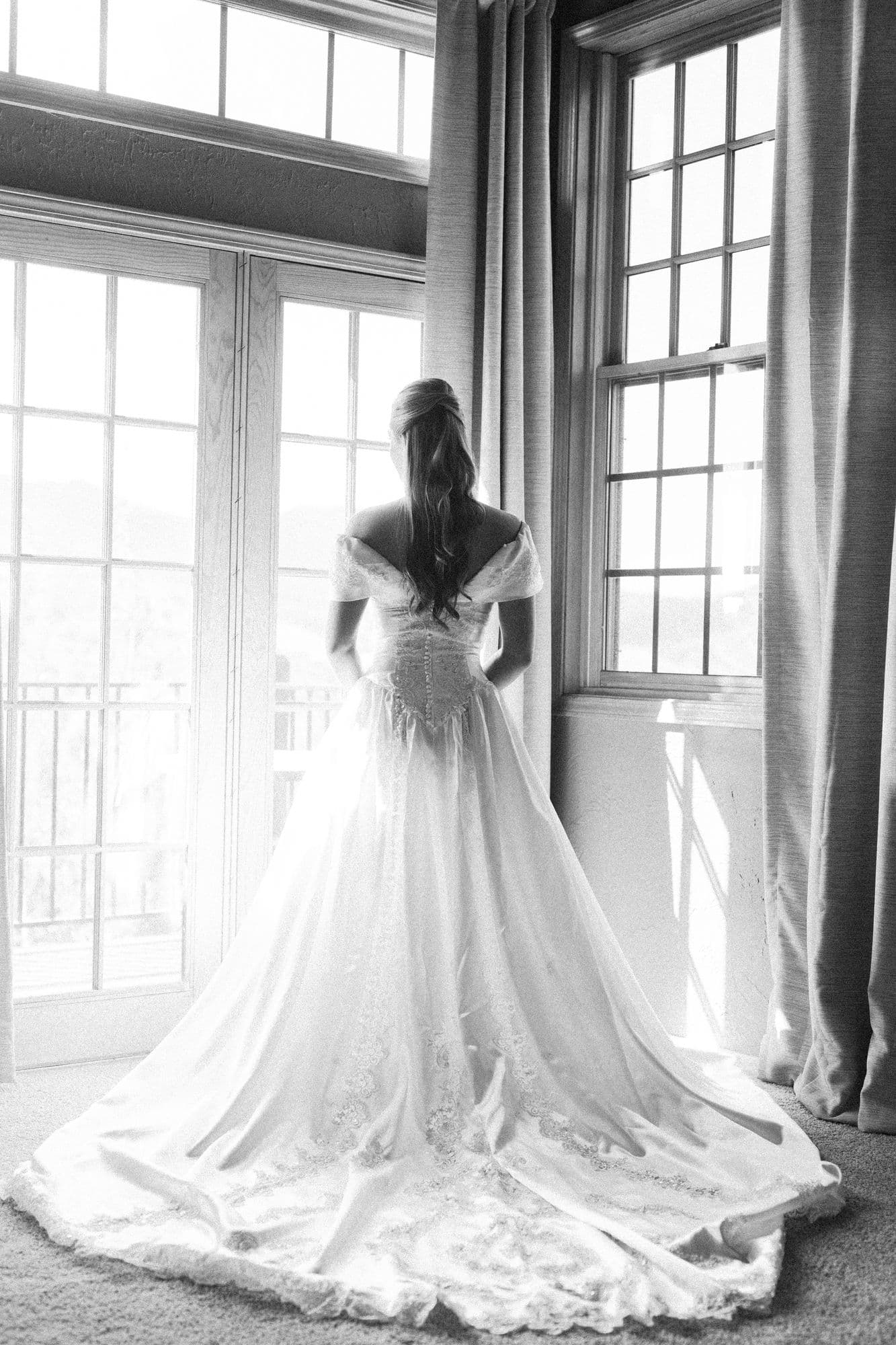 The back of Marita’s off-shoulder gown and its cathedral train in the window light, in black and white