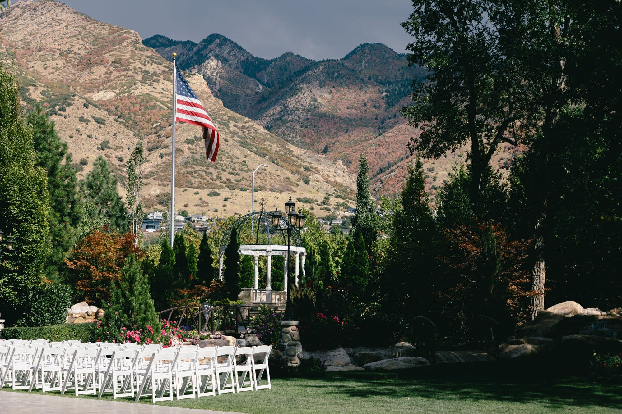 The ceremony lawn at Bellissimo Gardens at Tuscany in Salt Lake City, white chairs set in rows before a white colonnaded gazebo with the Wasatch mountains rising directly behind the garden