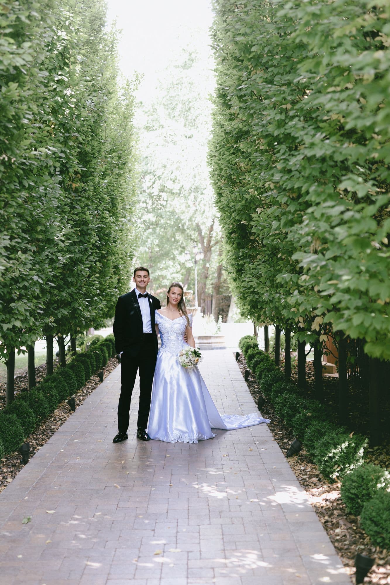 Kyle and Marita walking hand in hand down the cypress allée at Bellissimo Gardens in Salt Lake City