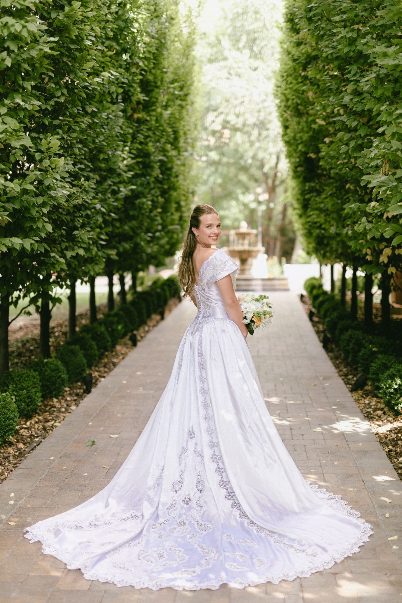 Marita alone in the cypress allée, her cathedral train spread the width of the brick path