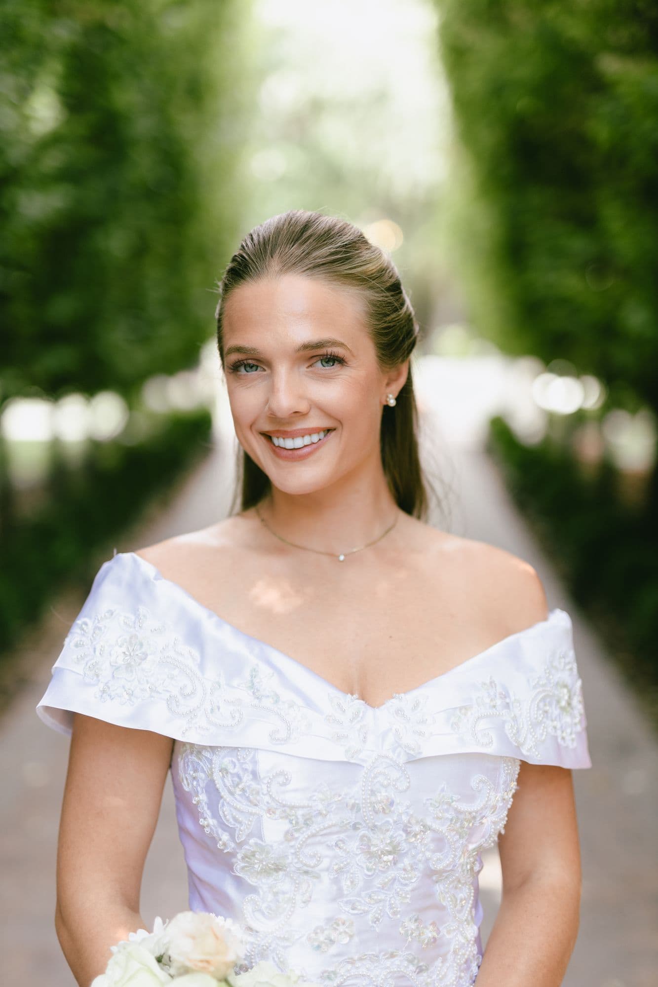 A close portrait of Marita in the cypress allée at Bellissimo Gardens, holding her white bouquet