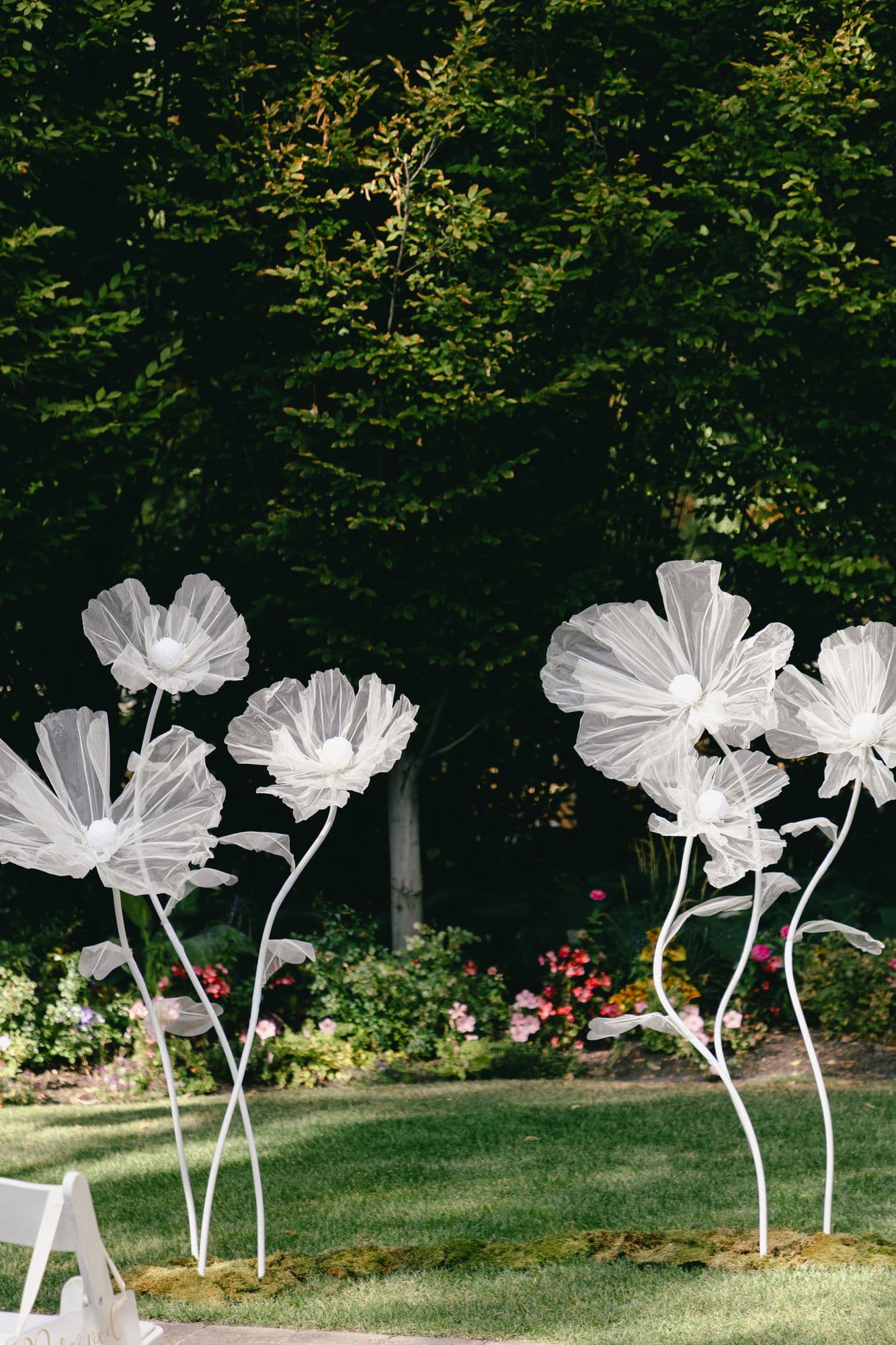 Oversized white paper flowers on curved wire stems standing at the ceremony site at Bellissimo Gardens