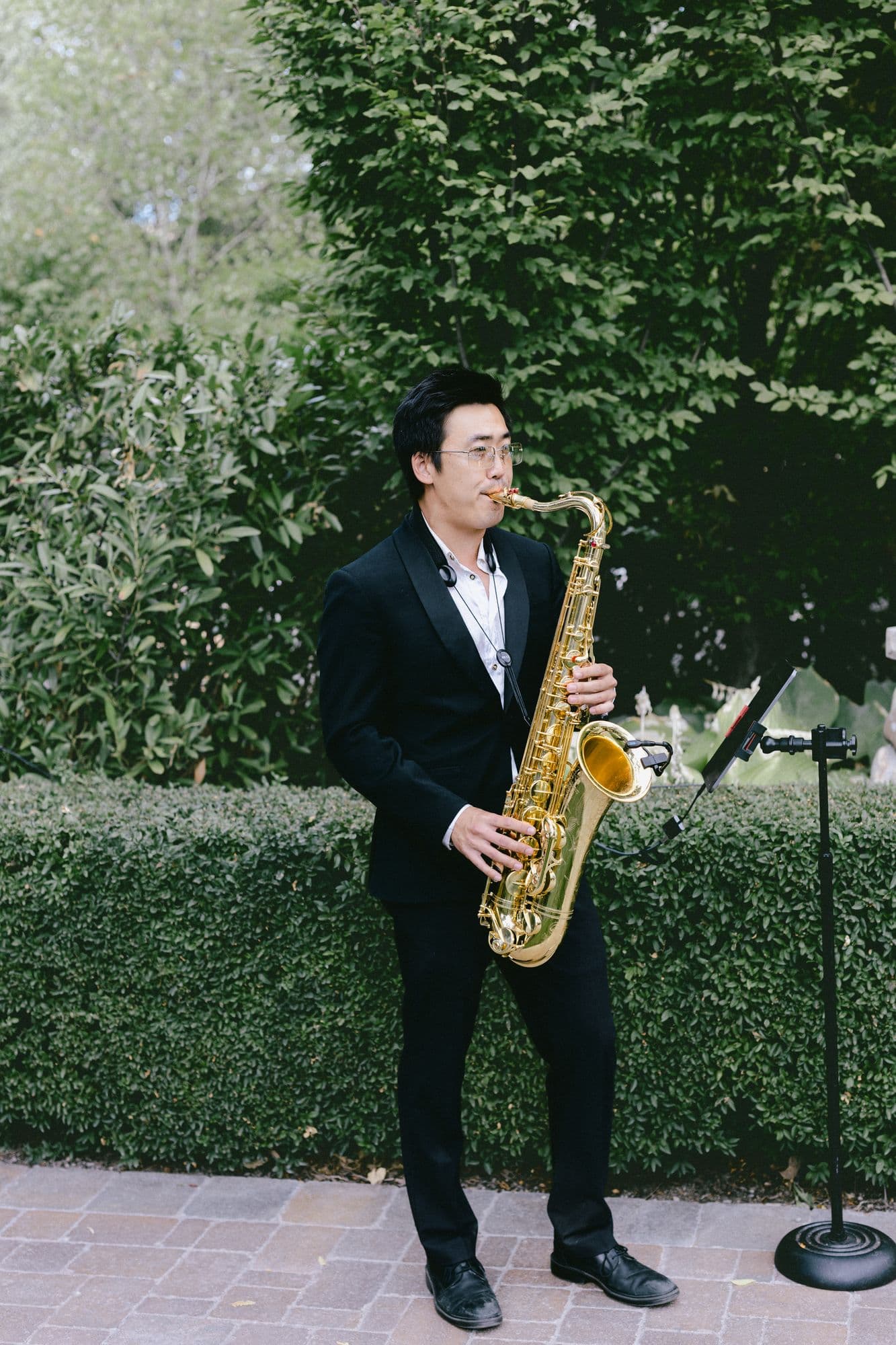 A saxophonist playing beside the hedge during the ceremony at Bellissimo Gardens