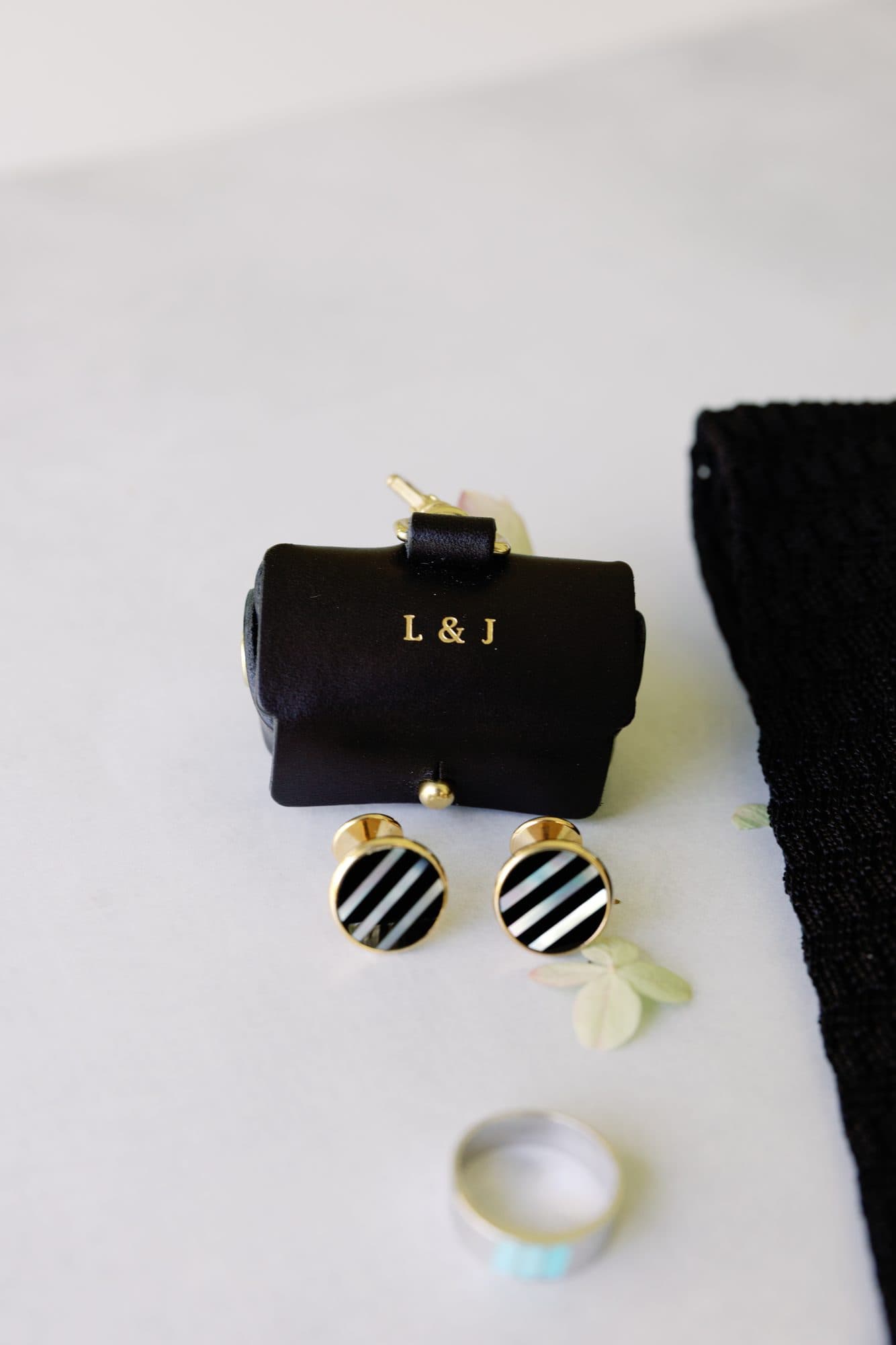 A small black leather case stamped L & J beside striped cufflinks and a wedding band