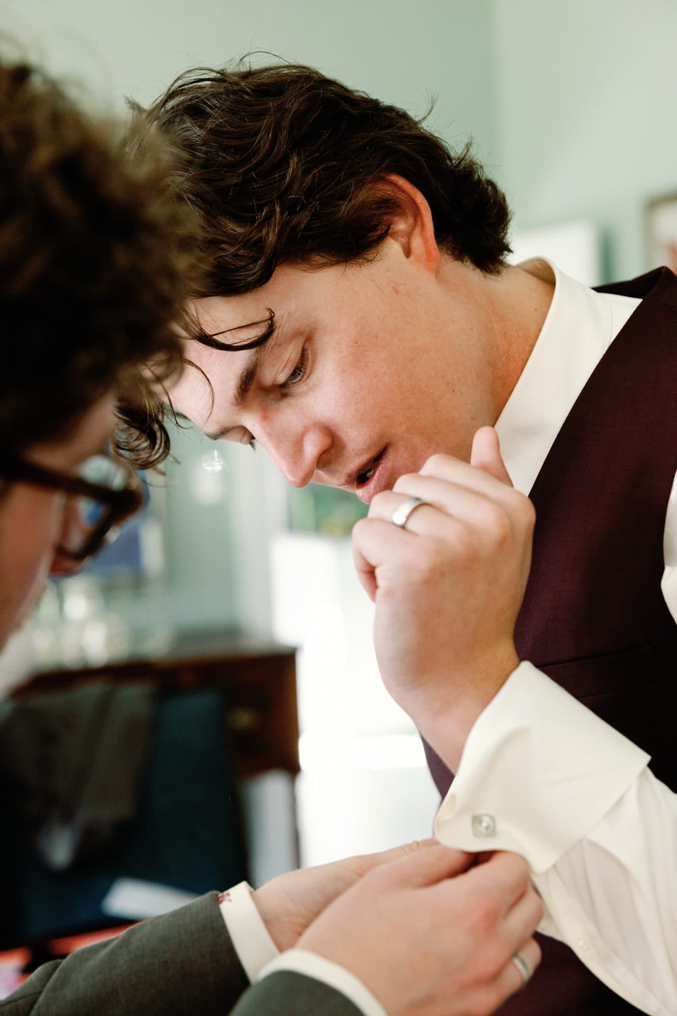 Jake in a burgundy waistcoat having his cuffs fastened by a friend