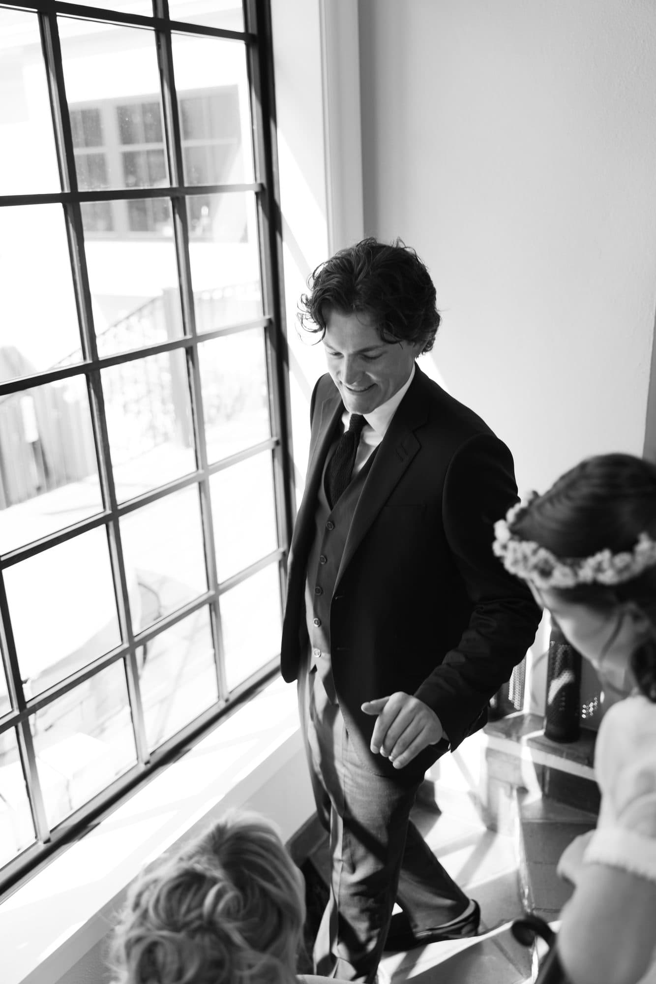 Jake in his suit beside a tall window before the ceremony, photographed in black and white