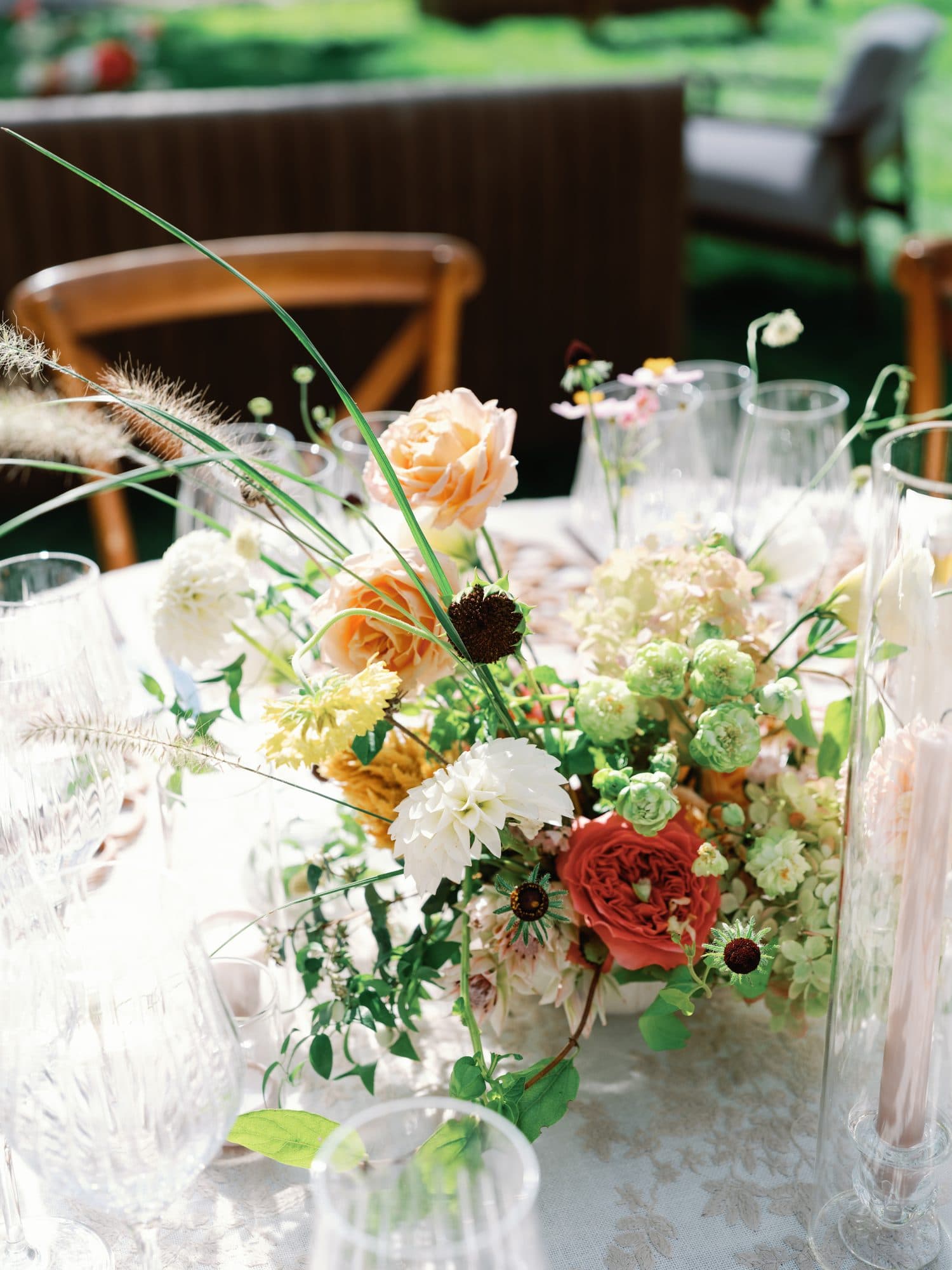 A centerpiece of peach roses, dahlias and long wild grasses on a reception table
