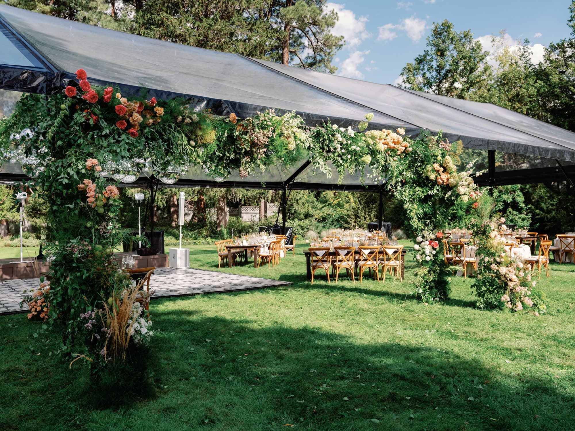 The clear-roofed reception tent on the lawn, its entrance framed in a floral arch of roses and greenery