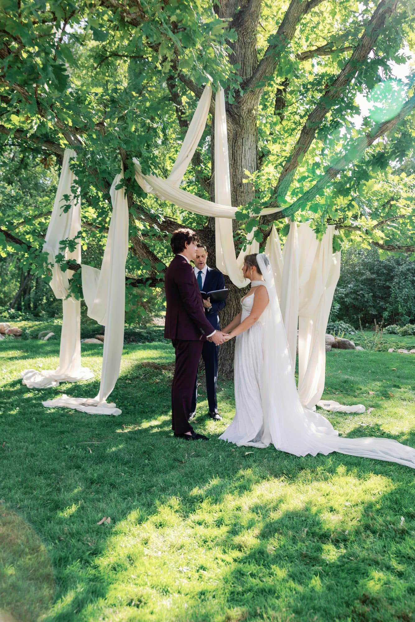 Lauren and Jake exchanging vows under an old tree hung with white fabric