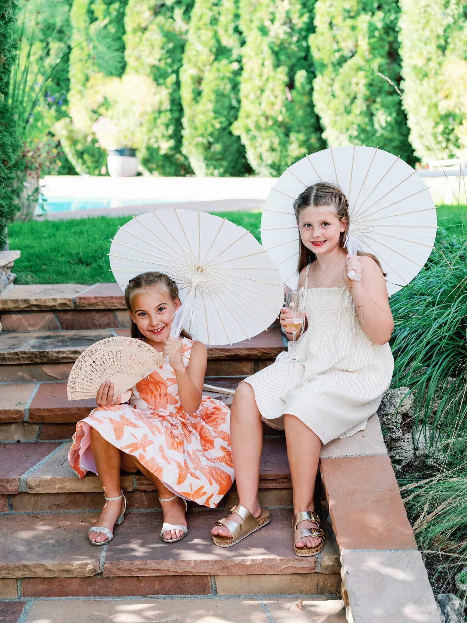 Two young guests sitting on the garden steps with white paper parasols