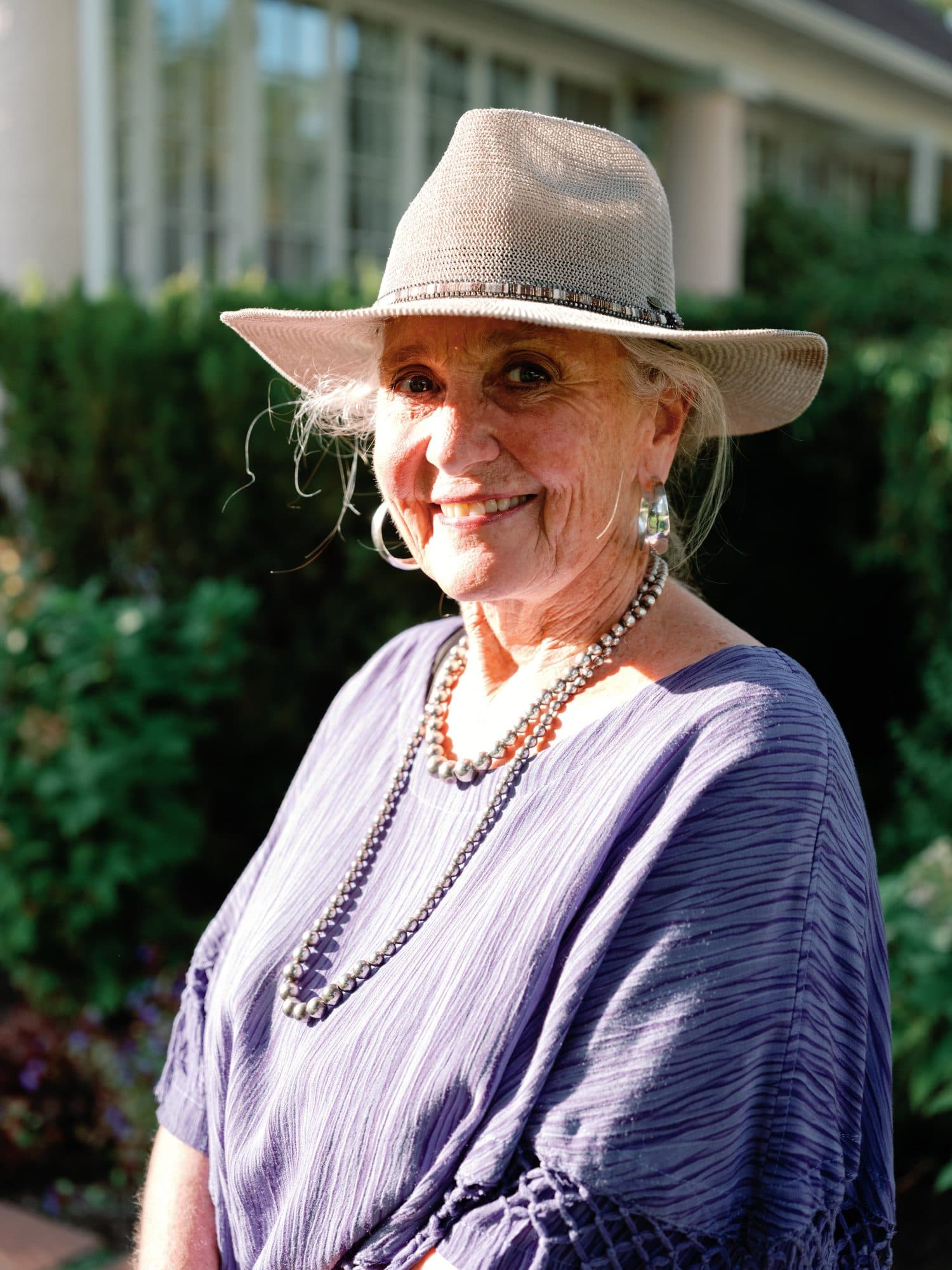A guest in a wide-brimmed hat and pearls smiling during cocktail hour