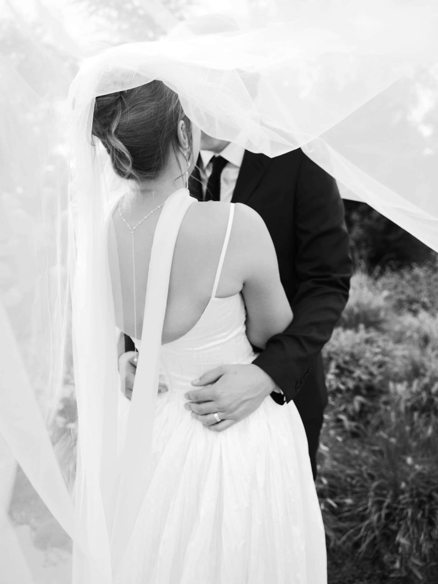 The veil lifting over Lauren and Jake in the garden, his hands at her waist, in black and white