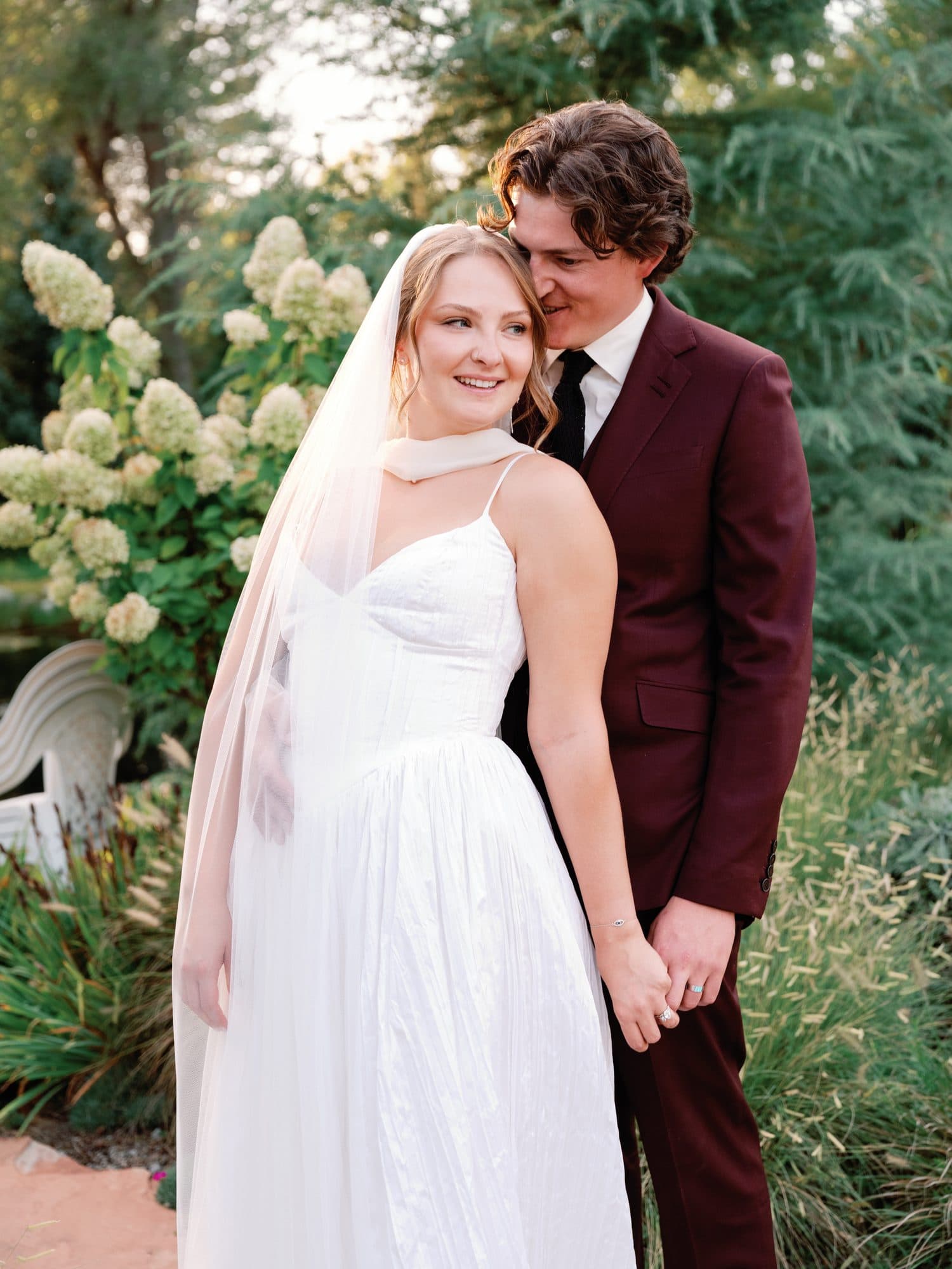 Jake whispering to Lauren as she laughs, white hydrangeas behind them