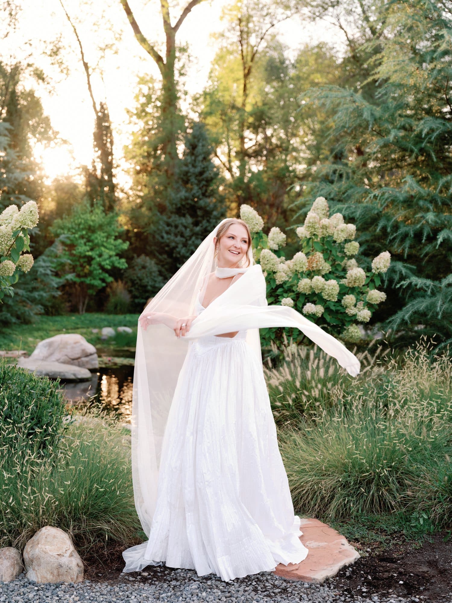 Lauren throwing her veil out in the garden as the evening sun comes through the trees