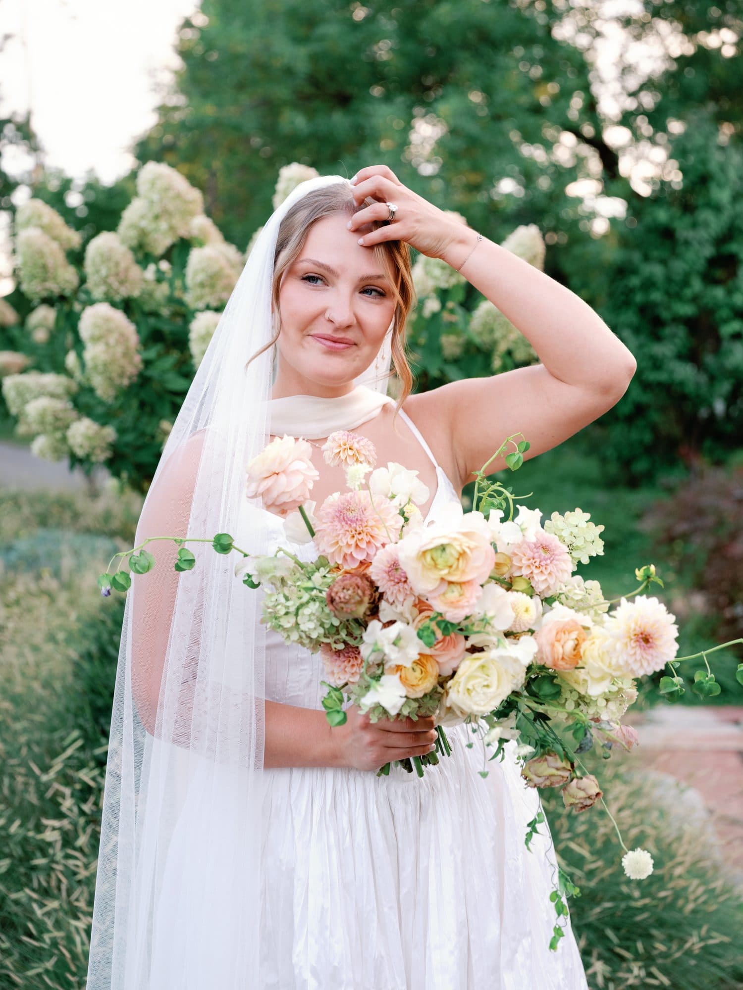 Lauren with one hand in her hair, holding her bouquet among white hydrangeas