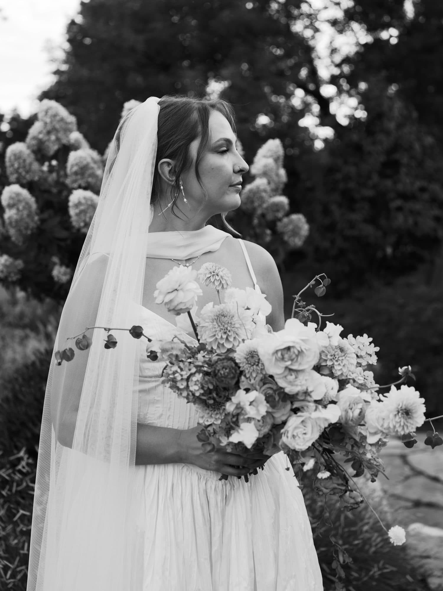 Lauren in profile with her bouquet, her veil falling past her shoulders, in black and white