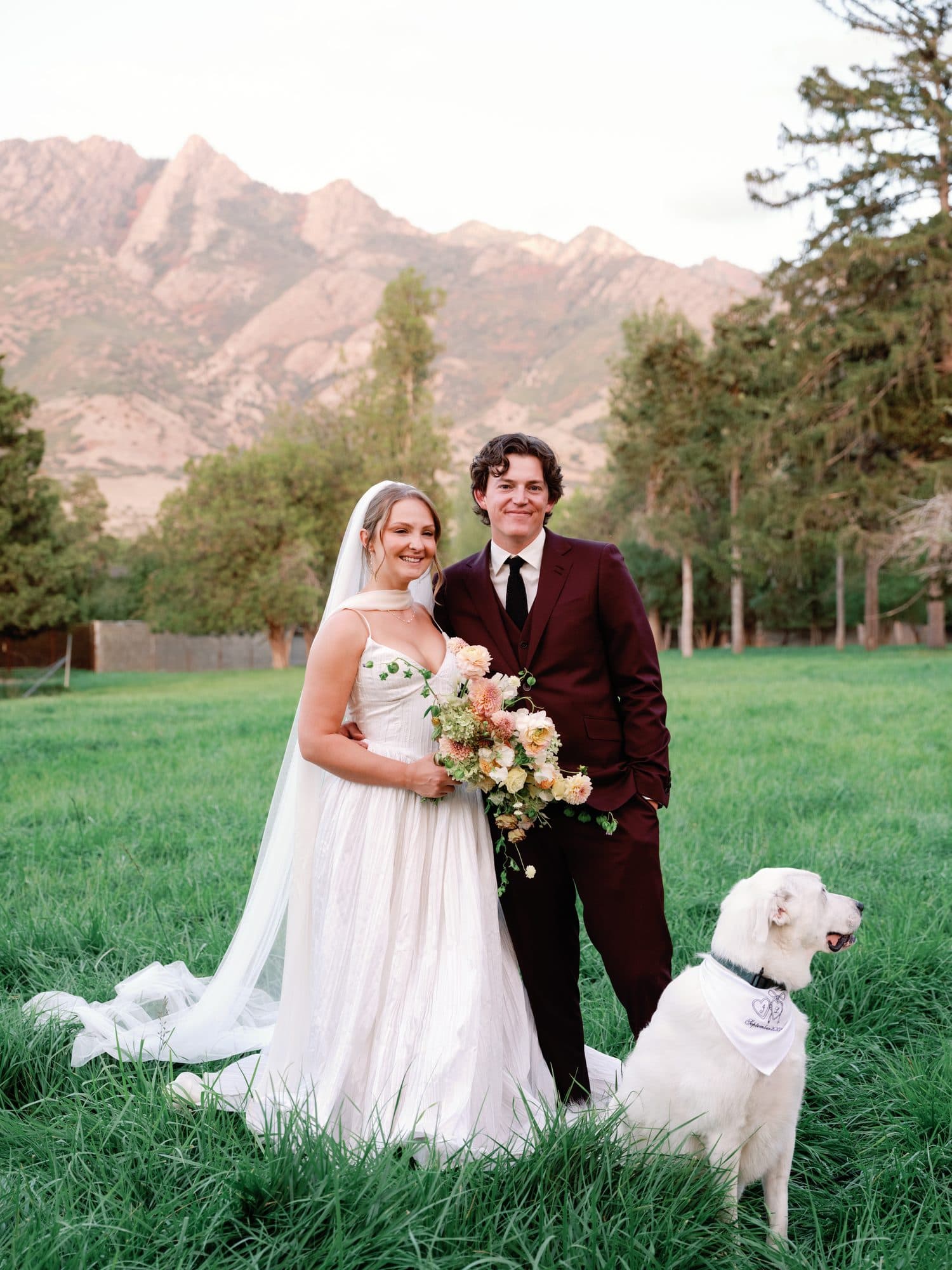 Lauren and Jake in a meadow under the mountain, the white dog at their side
