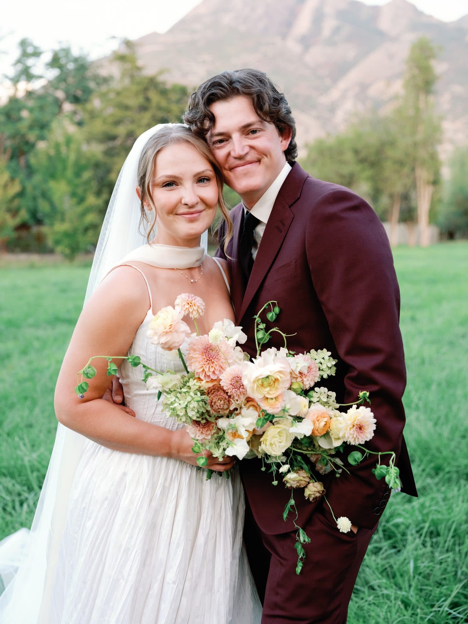 Lauren and Jake cheek to cheek in the meadow with her bouquet, the mountain behind them