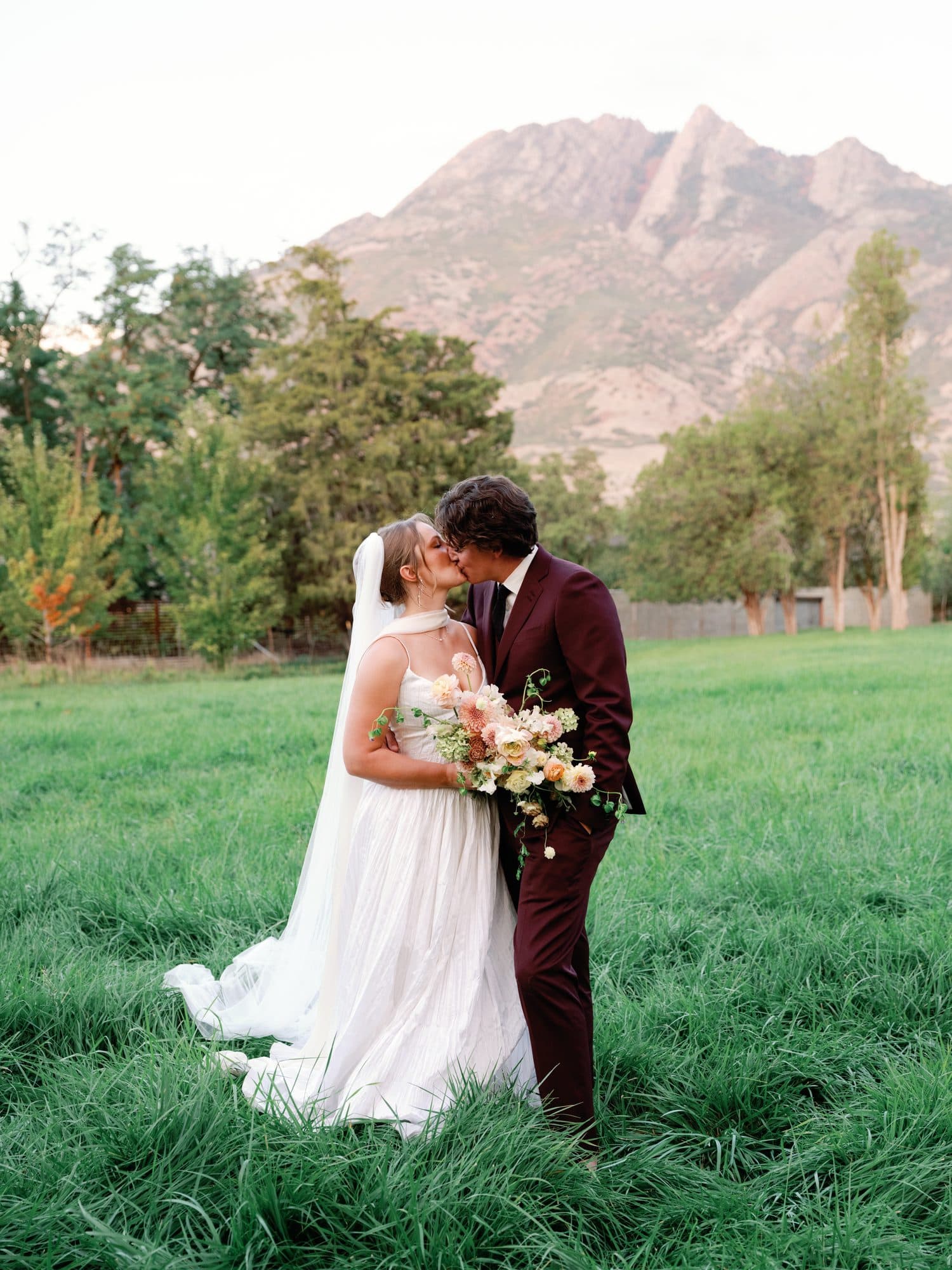 Lauren and Jake kissing in the long grass of the meadow below the mountain