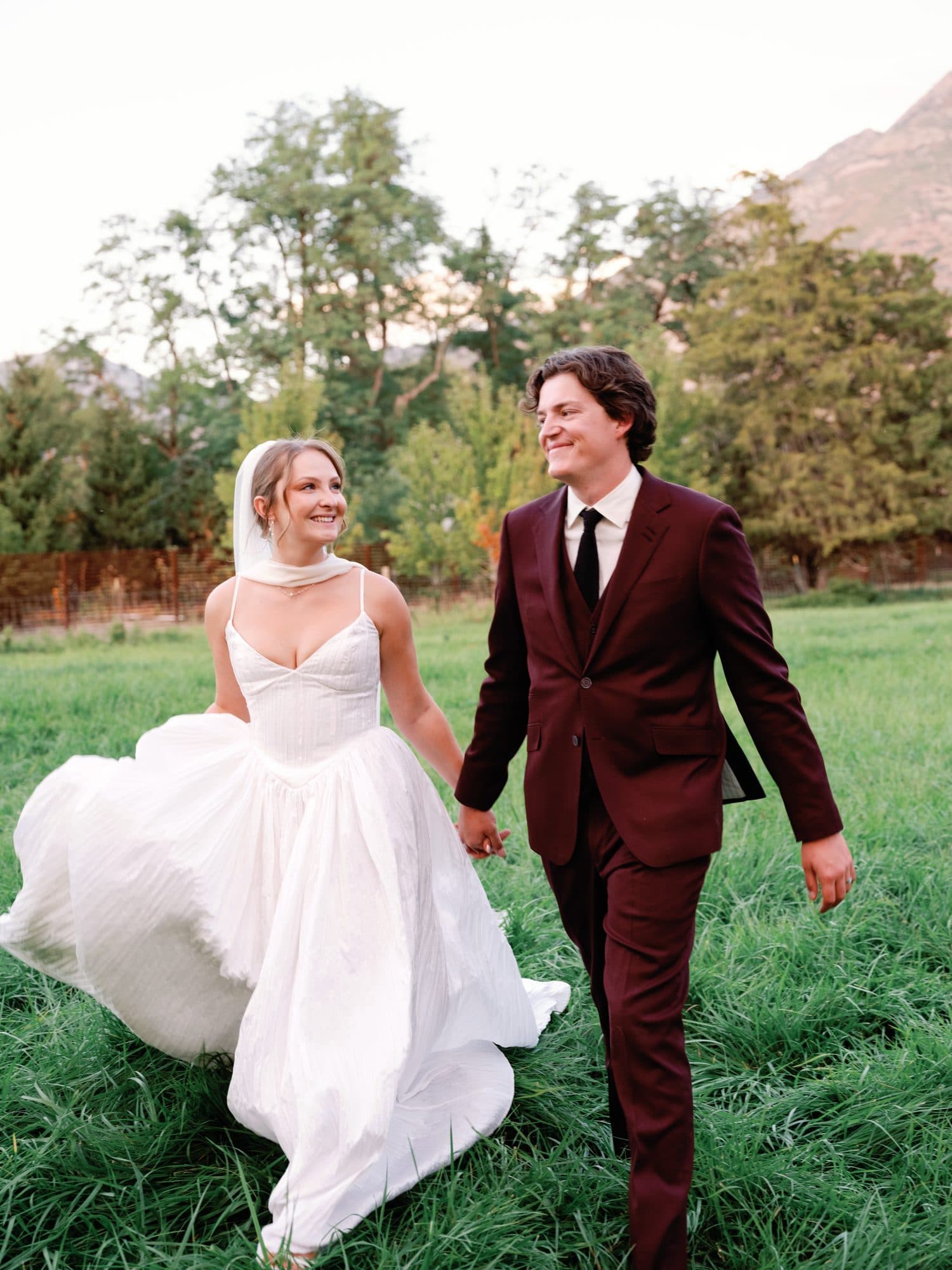 Lauren and Jake walking hand in hand through the meadow, her skirt swinging