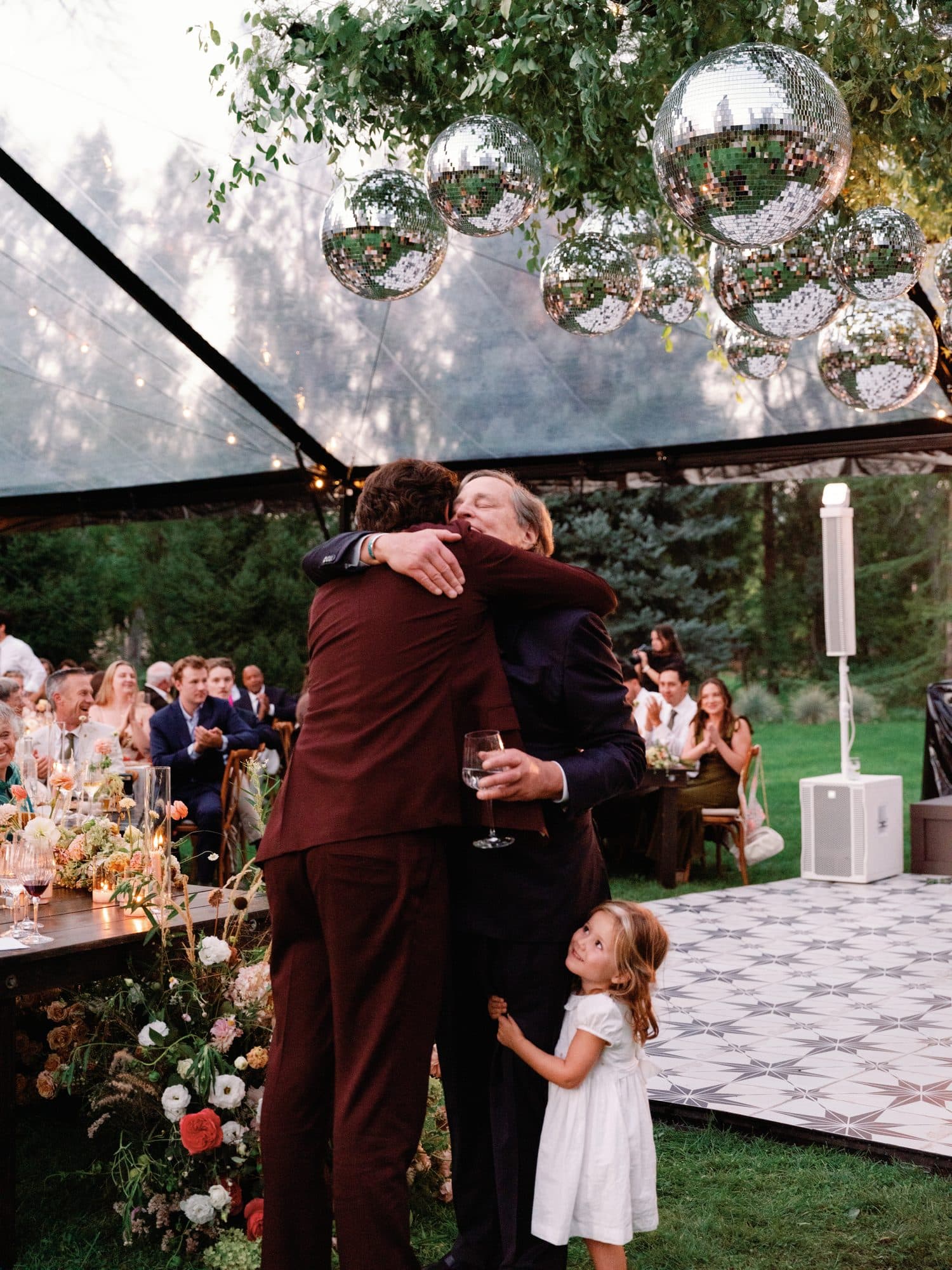 Jake hugging a guest after a toast while a little girl in white holds on and looks up at them