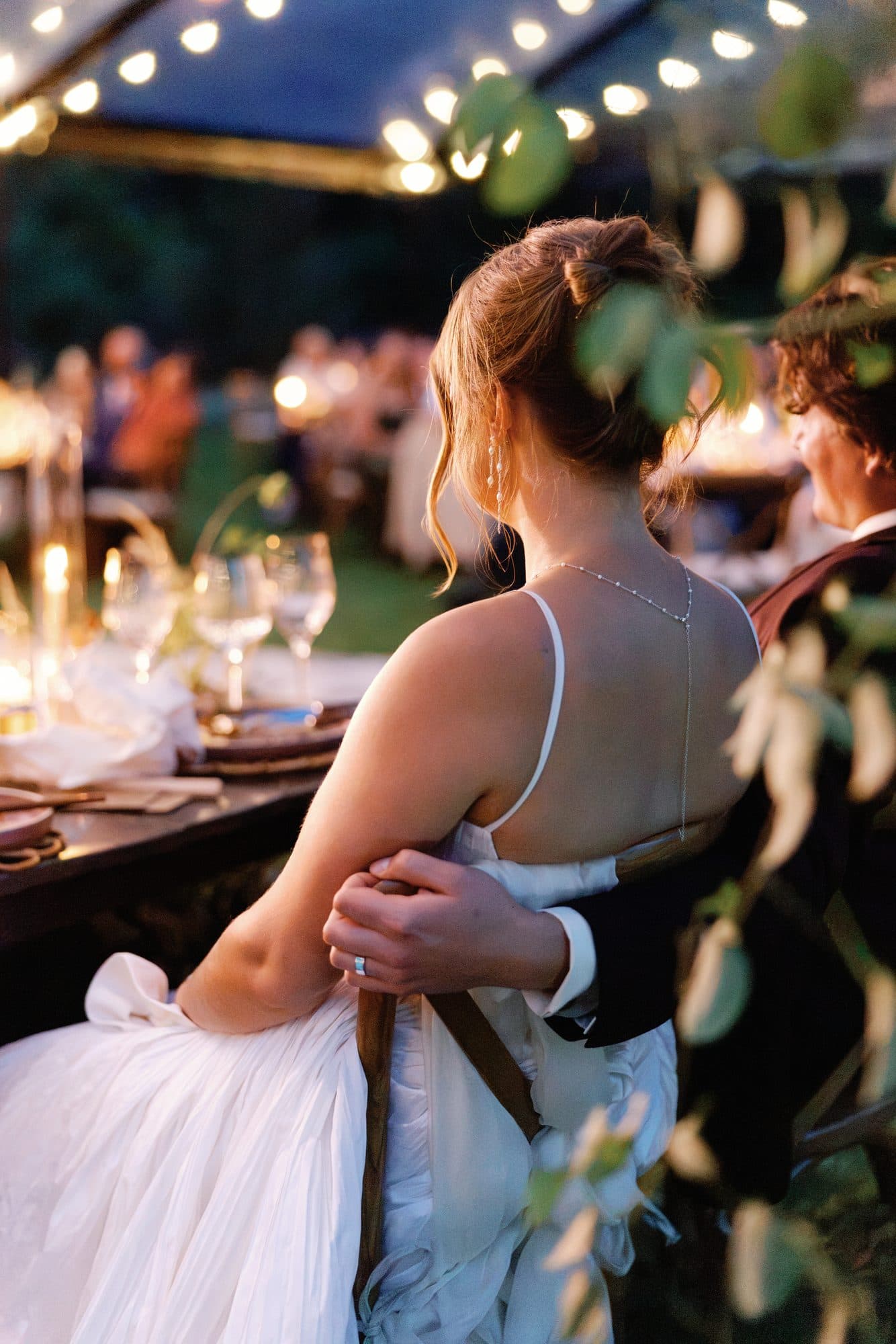 Lauren at the candlelit table at dusk with Jake’s arm around her waist, seen through the leaves