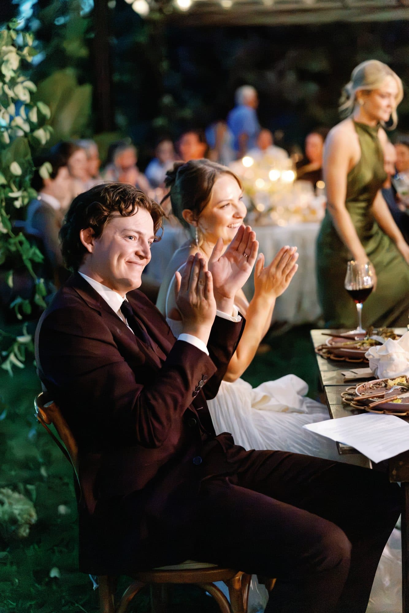 Jake grinning and Lauren clapping from their table during the toasts