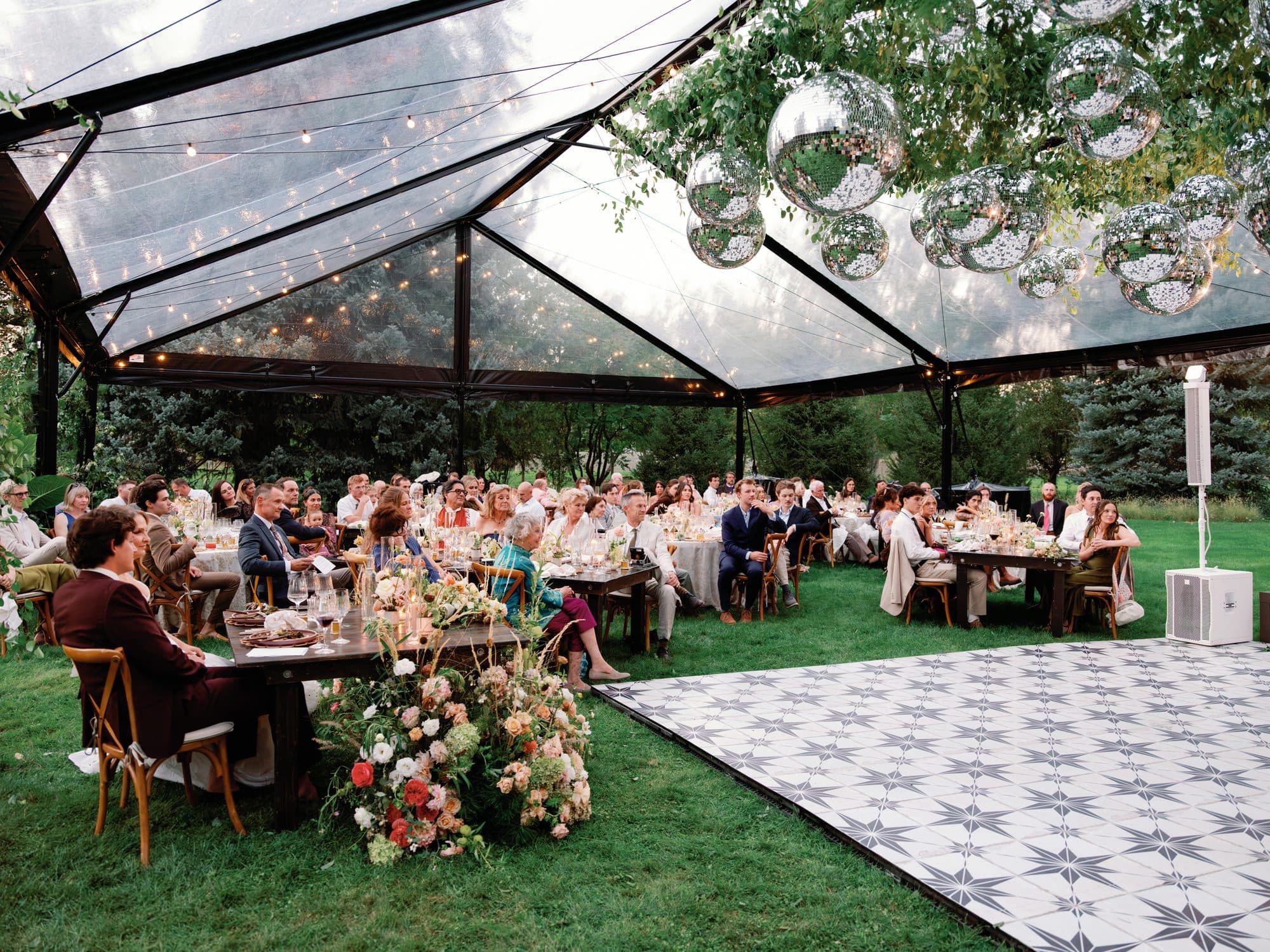 The tent at dusk during dinner: mirrored disco balls in the greenery overhead, a meadow of flowers at the head table and the star-tiled dance floor