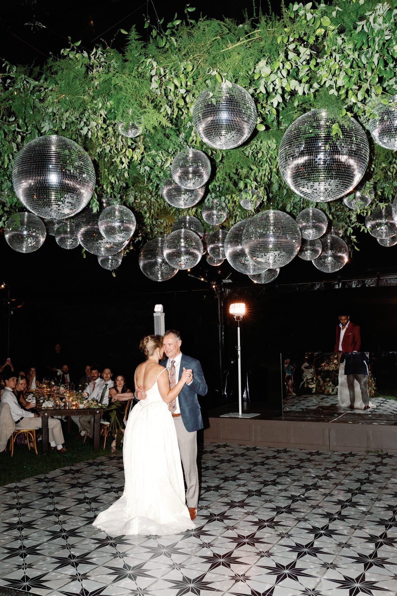 Lauren dancing with her father on the star-tiled floor beneath a ceiling of mirrored disco balls and greenery