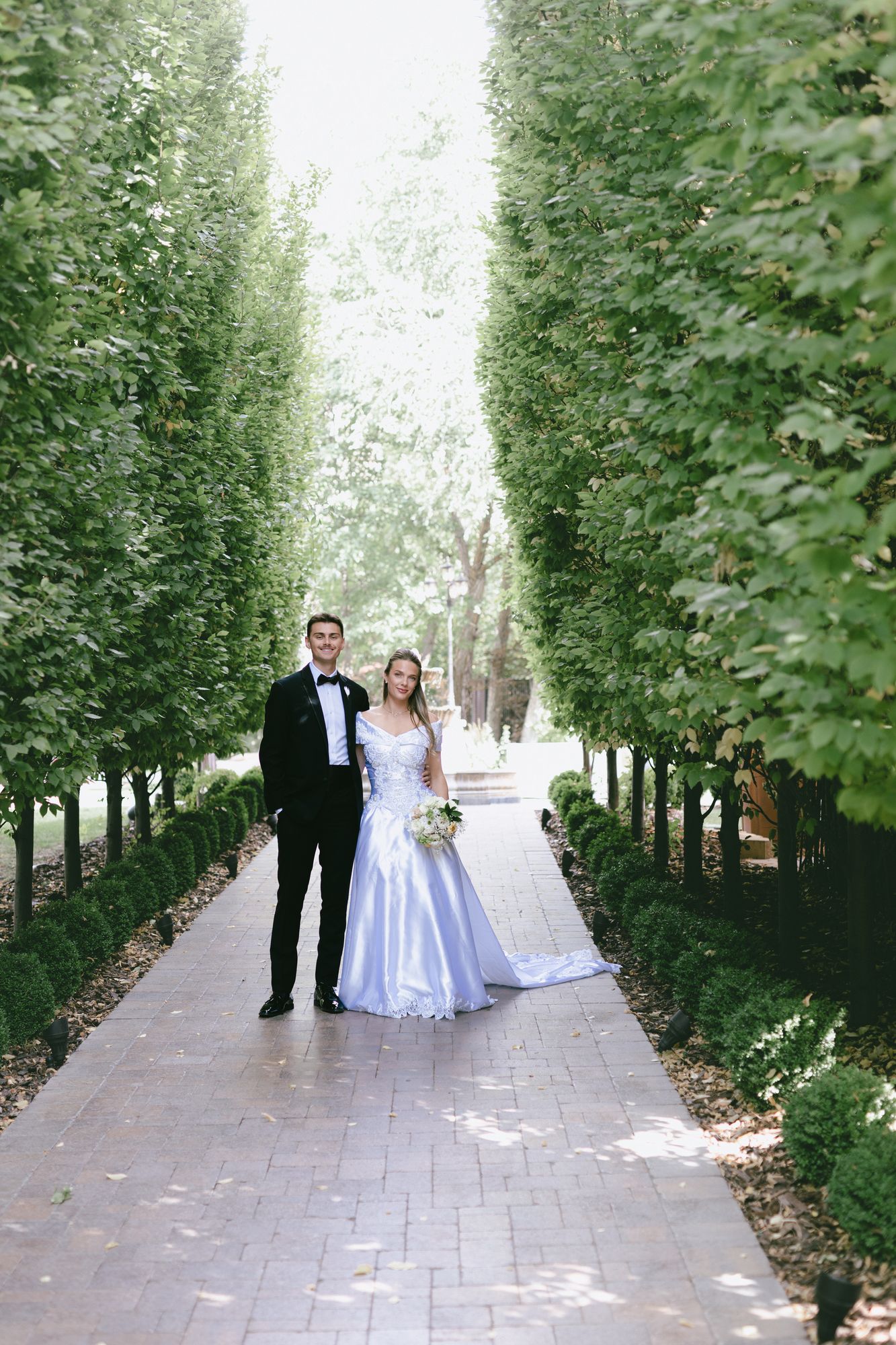 Kyle and Marita walking hand in hand down the cypress allée at Bellissimo Gardens in Salt Lake City