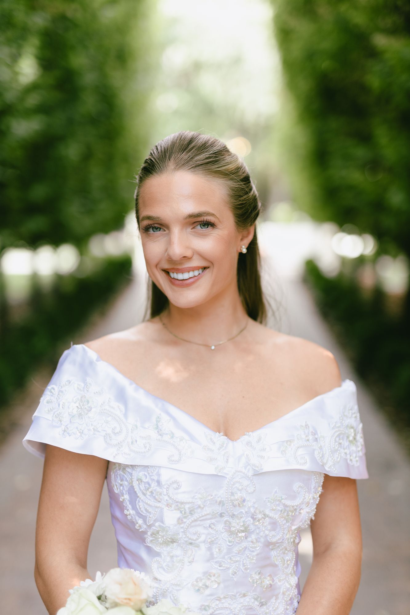 A close portrait of Marita in the cypress allée, holding her white bouquet