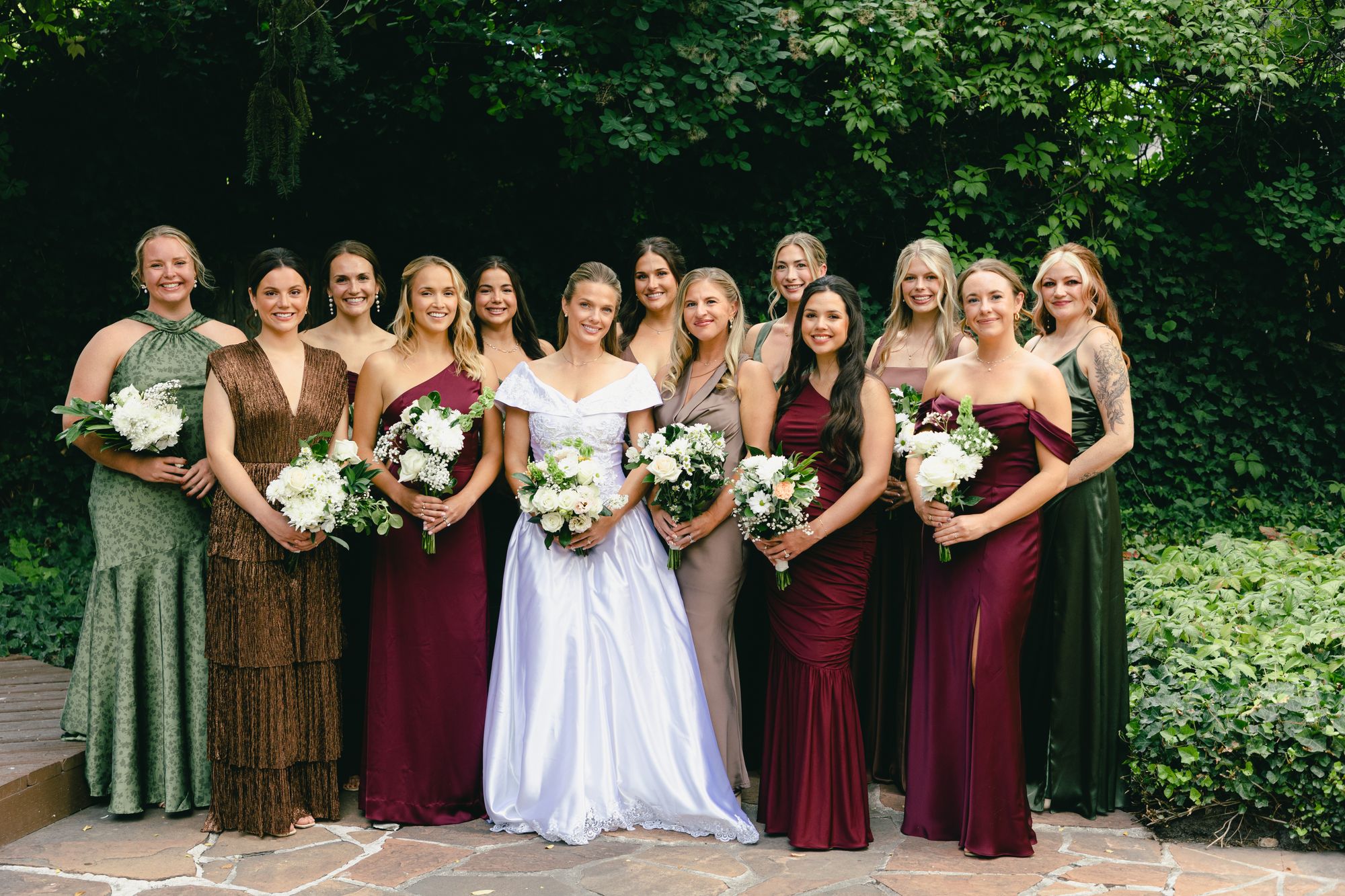 Marita’s bridesmaids in olive, burgundy, brown and gold gowns with white bouquets