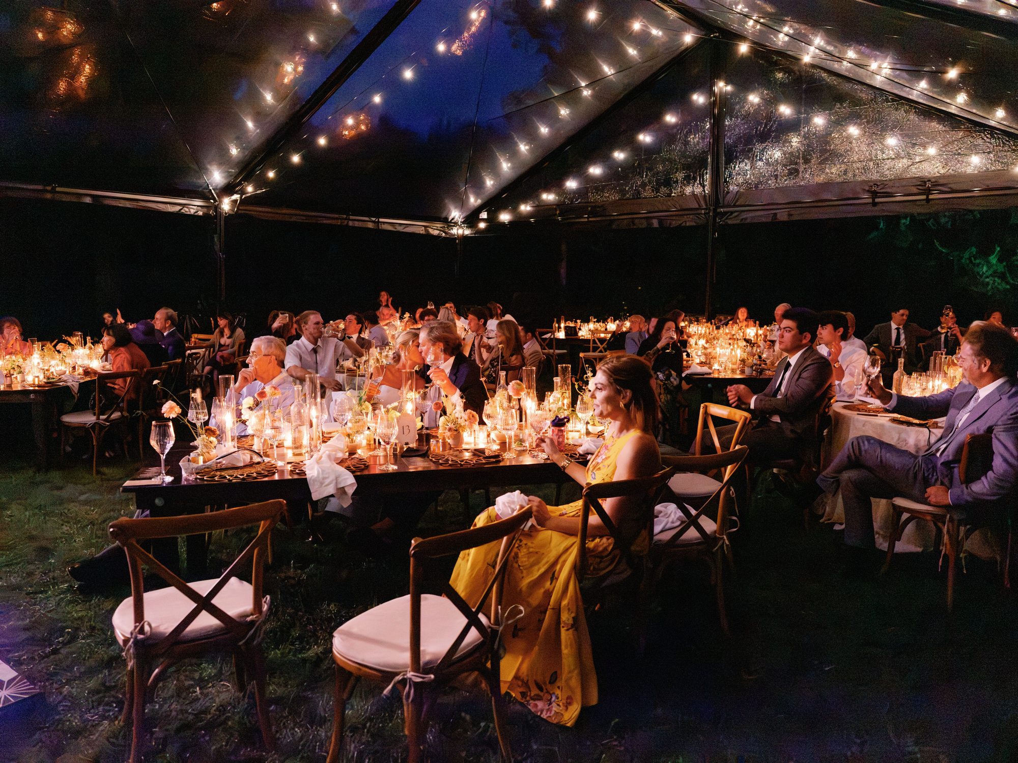 A clear-roofed reception tent at night, lit by candles and string lights, wedding photography by Christopher Cook