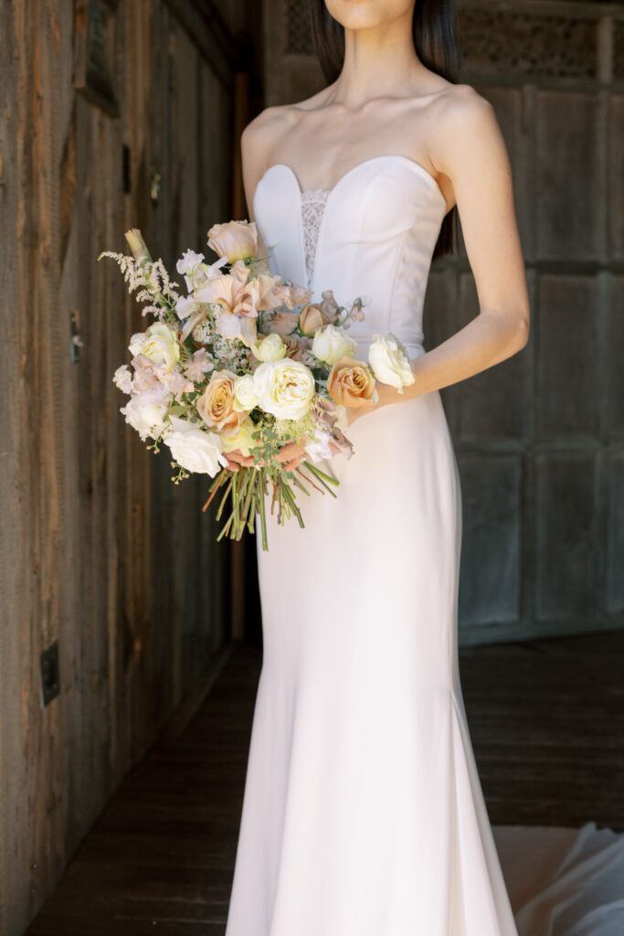 A stunning bride adorned in a chic Pronovias gown stands gracefully in the remuda at The Lodge at Blue Sky, enveloped by the rustic ambiance of warm wood beams and bathed in the glow of natural sunlight.
